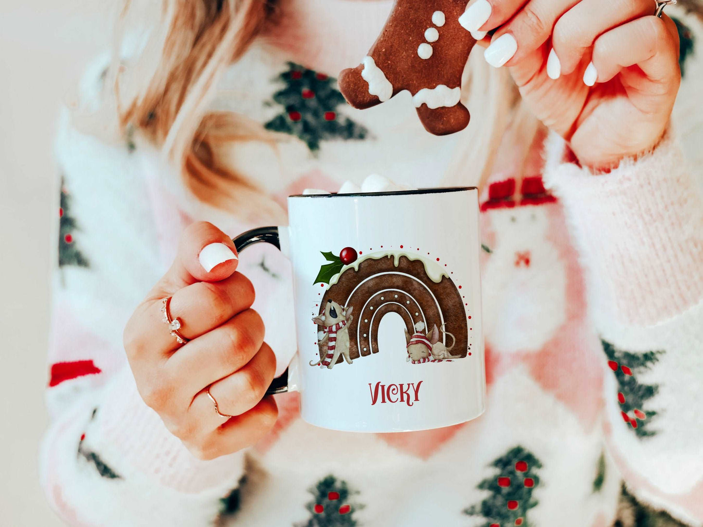 woman holding a white mug with a black handle. The mug has a cute christmas pudding and mouse design printed on it with a name below