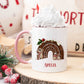 white mug with a pink handle in a christmas scene. The mug has a cute christmas pudding and mouse design printed on it with a name below