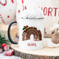 white mug with a black handle in a christmas scene. The mug has a cute christmas pudding and mouse design printed on it with a name below