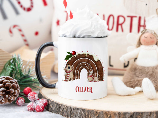 white mug with a black handle in a christmas scene. The mug has a cute christmas pudding and mouse design printed on it with a name below