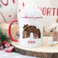 white mug with a red handle in a christmas scene. The mug has a cute christmas pudding and mouse design printed on it with a name below