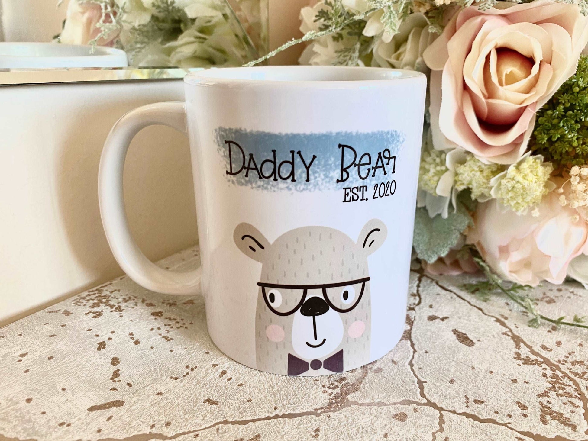 white mug with a bear illustration printed on and the text daddy bear est. 2020 printed over a blue brushdtroke above.