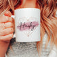woman holding a white mug with a rose gold geometric heart and pink brush stroke design with a black script name printed over the top