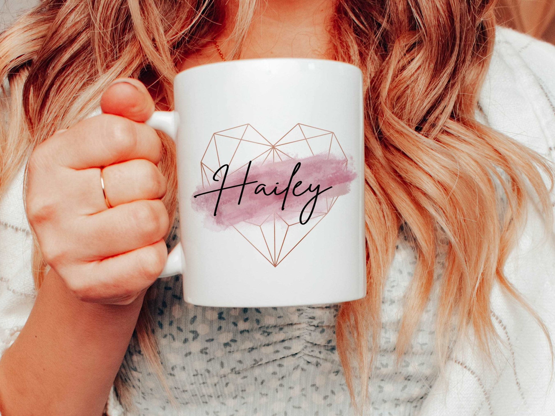 woman holding a white mug with a rose gold geometric heart and pink brush stroke design with a black script name printed over the top