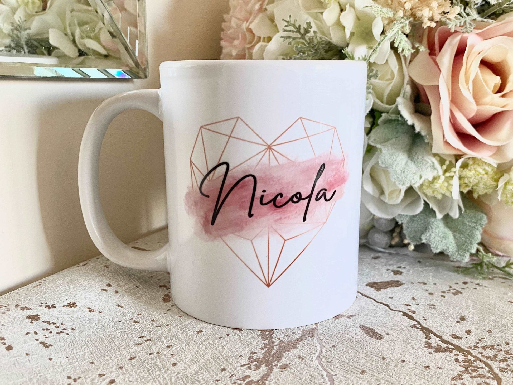 white mug with a rose gold geometric heart and pink brush stroke design with a black script name printed over the top
