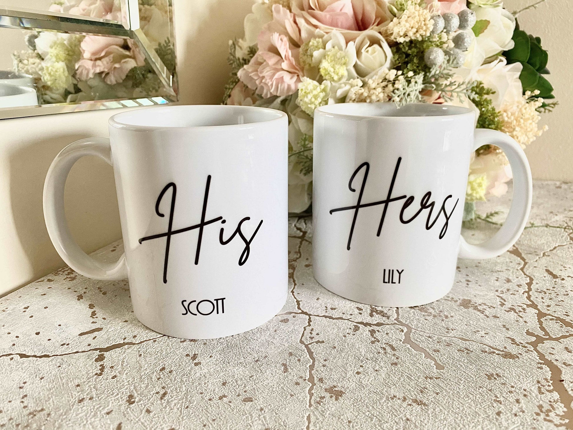 set of two white mugs. One has the text His in a script font with a name below and the other has Hers with a name below.