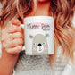 woman holding a white mug with a bear illustration on with the text mummy bear est. 2022 printed above over a pink brush stroke.