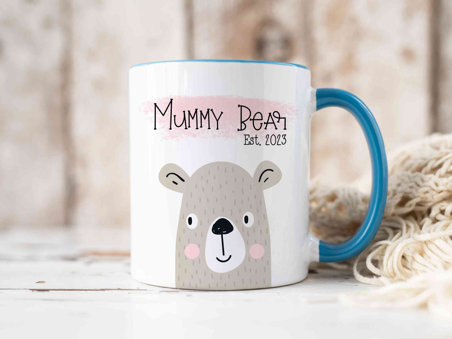 White mug with blue handle sitting on a worktop. The mug has a cute bear design printed on it with the text mummy bear above