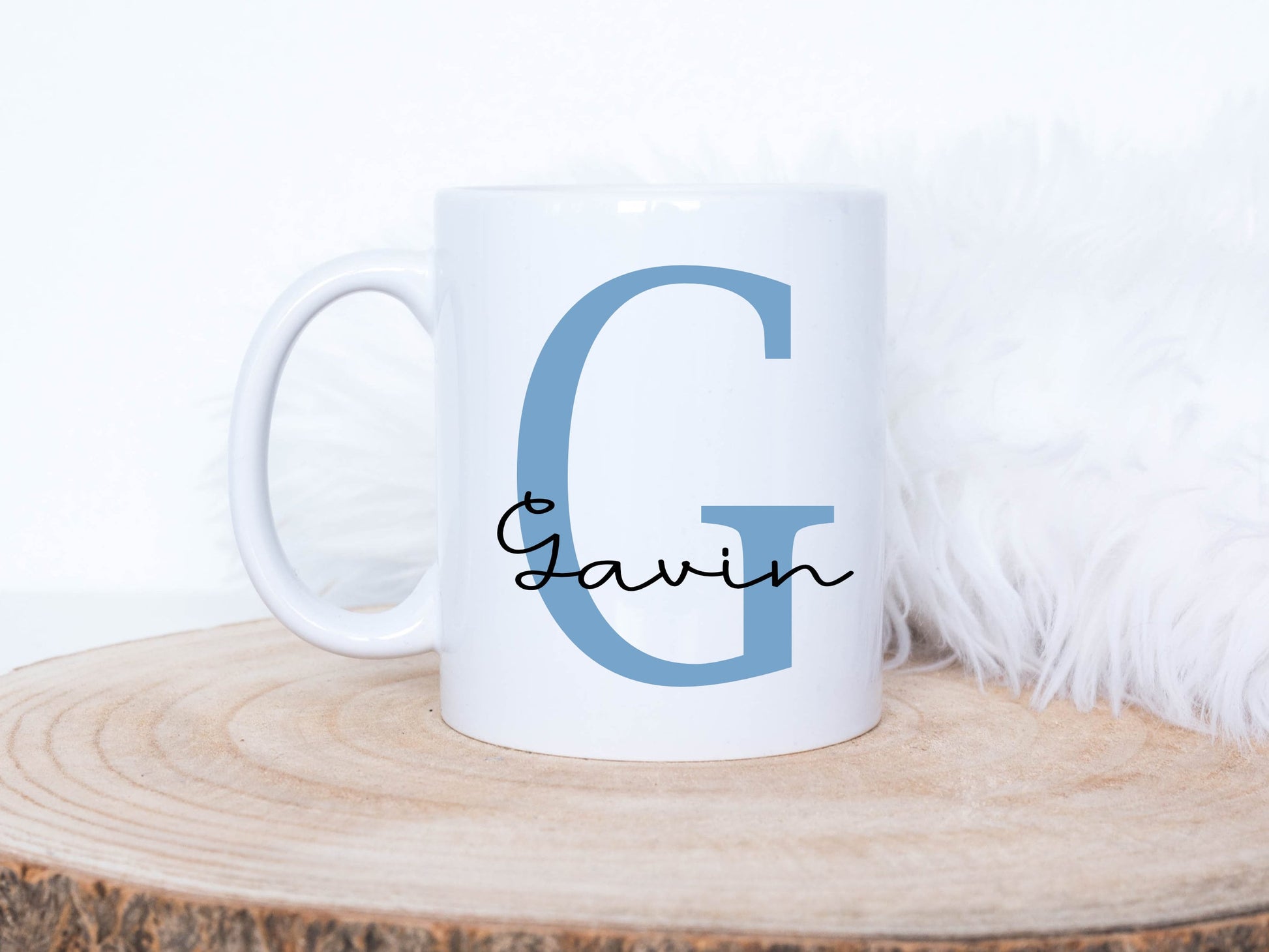 white mug on a log slice has a large blue letter G printed on it with the name Gavin printed over in a black script font