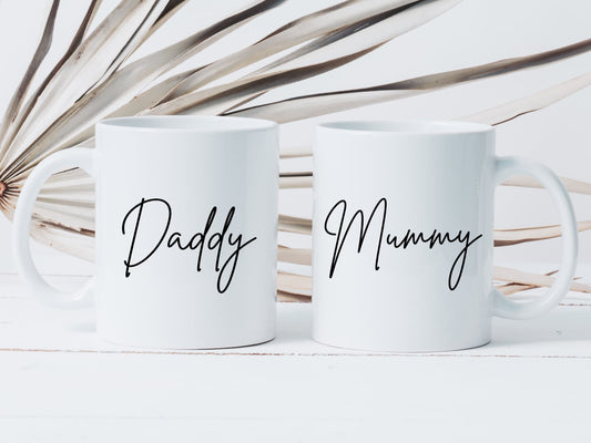 two white mugs on a white surface. One has the text daddy printed on in a script font, the other has mummy printed on