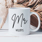 white mug with the text Mr printed in a script font. There is a surname beneath in a smaller font