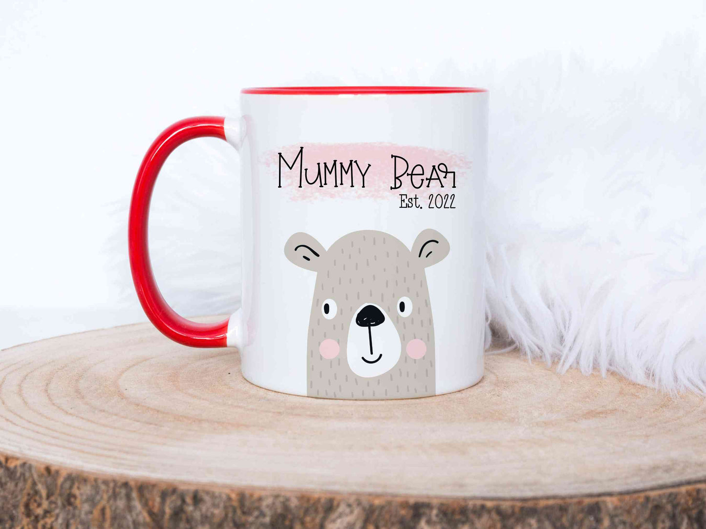 mummy bear design printed on a white mug with red handle. The mug is sitting on a wood slice in front of a white fluffy background