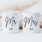 two white mugs on a white surface. One mug has the text Mr printed on in a script font with a surname below. The other has the text Mrs