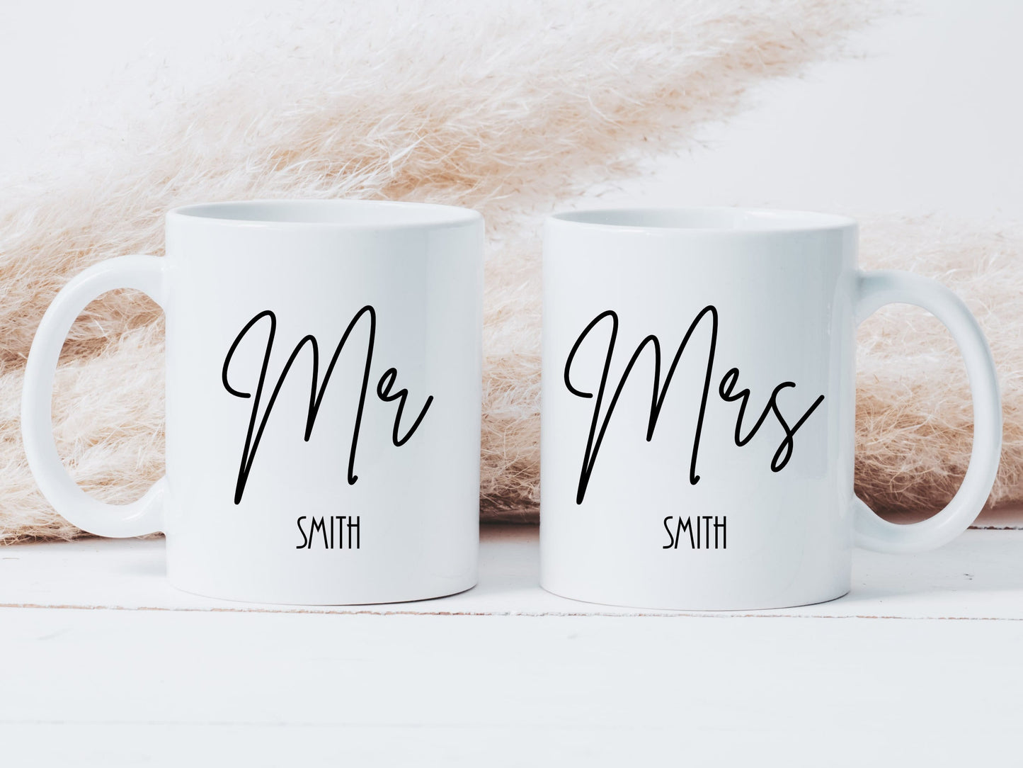 two white mugs on a white surface. One mug has the text Mr printed on in a script font with a surname below. The other has the text Mrs